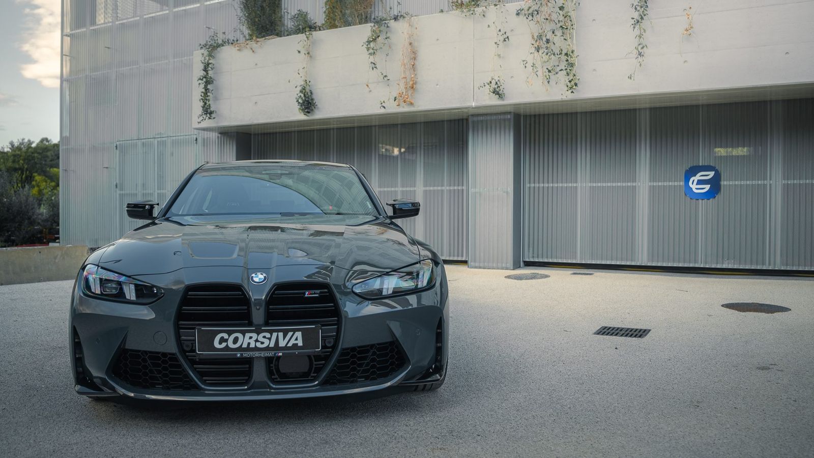 BMW M3 Compétition Corsiva garée devant les box de l'agence, à Chambéry