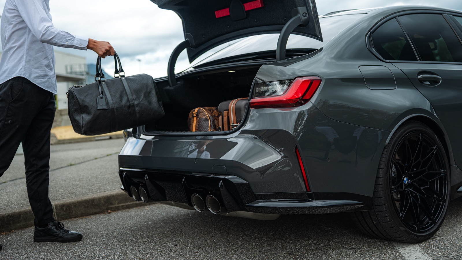 Sac de voyage glissé dans le coffre d'une BMW M3 Compétition Corsiva, prête à partir de Chambéry vers Lyon