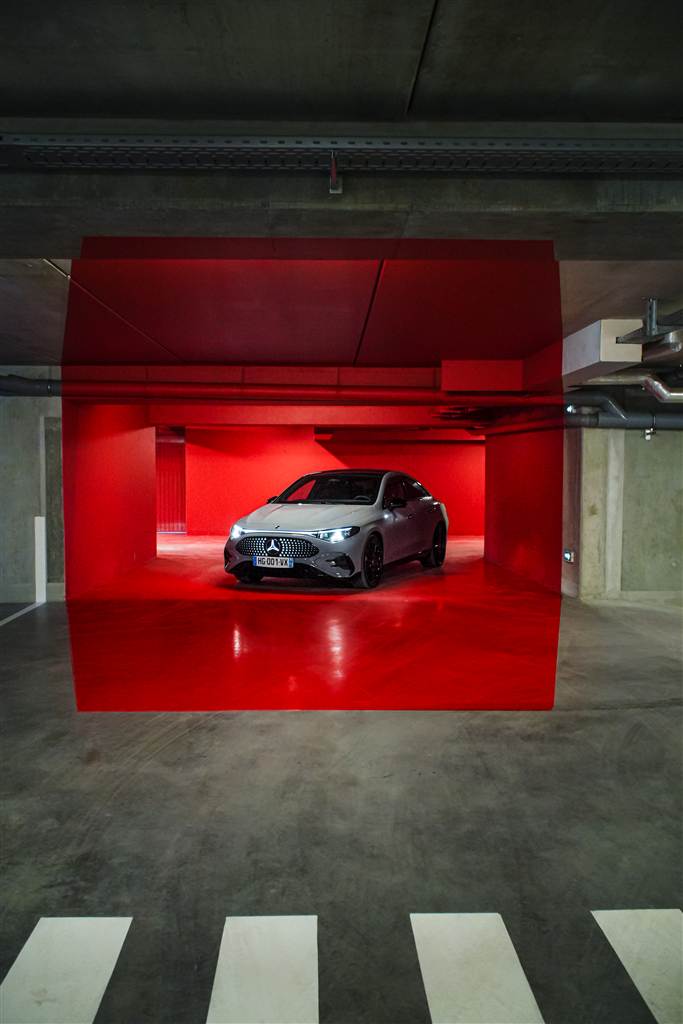 Mercedes-Benz CLA AMG grise, phares allumés, dans un parking aux murs peints en rouge