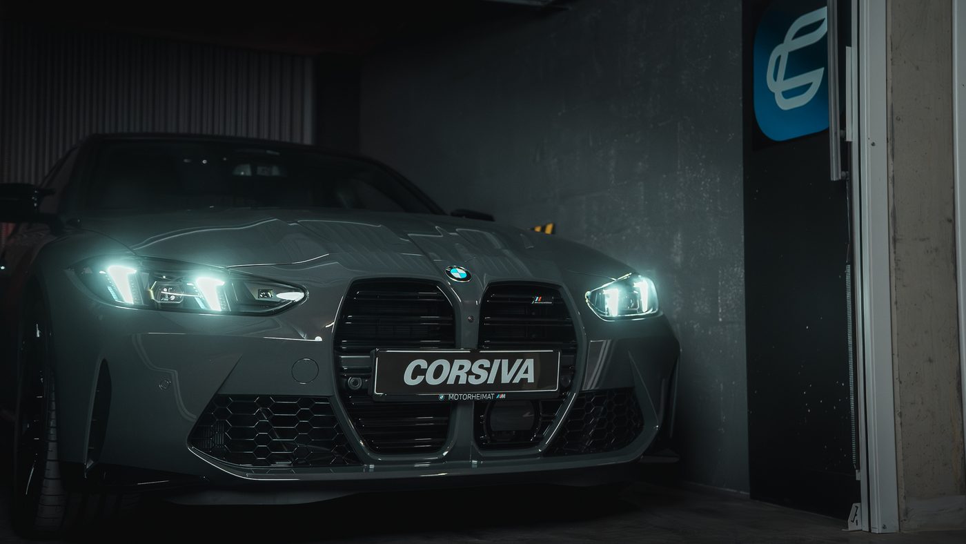 BMW M3 Compétition Corsiva, phares allumés, dans un box de l'agence à Chambéry